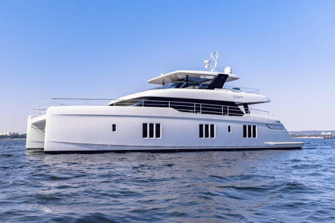 A sleek white catamaran yacht glides across the calm blue water under a clear sky.