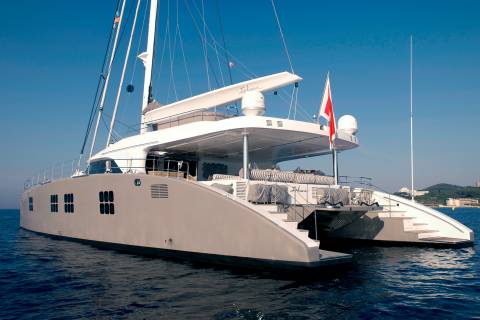 A sleek, modern catamaran glides through calm blue waters under a clear sky.