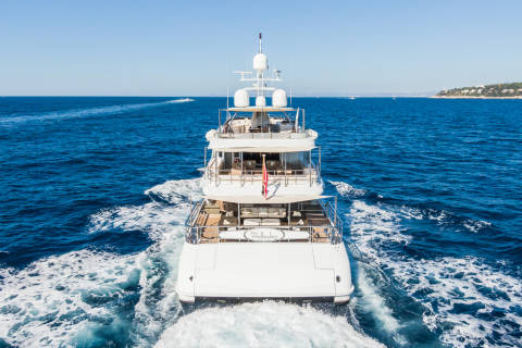 A luxurious white yacht cuts through the deep blue ocean, leaving a foamy wake under a clear sky.