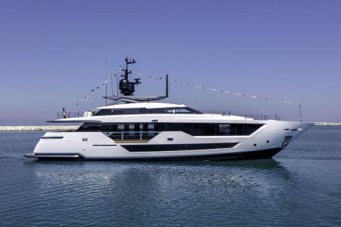 A sleek white yacht glides through calm blue waters under a clear sky, adorned with festive flags.