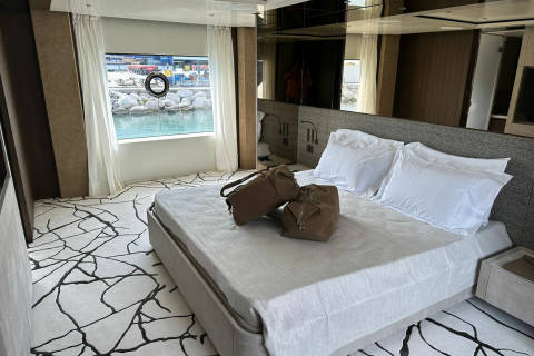 Two stylish duffel bags rest on a neatly made bed in a luxurious cabin with a view of the harbor.