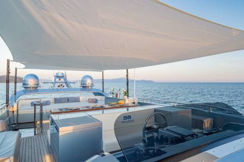 A luxurious yacht with a shaded deck overlooking a serene ocean landscape under a clear blue sky.