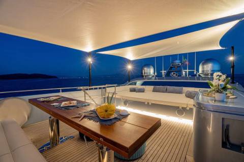 A luxurious yacht deck with a cozy seating area, a wooden table, and a stunning view of the ocean in the background.