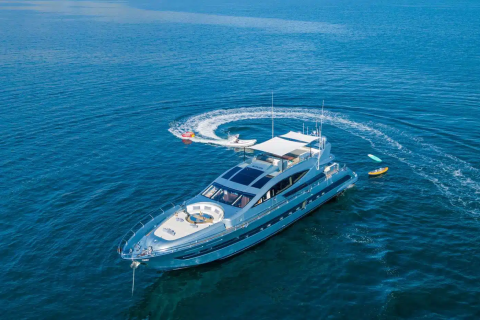 A large white yacht is sailing across the calm, deep blue waters of the ocean, leaving a trail of white foam in its wake.