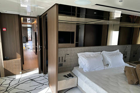 Luxurious hotel suite features a king-sized bed with crisp white linens, modern mirrored wardrobes, and a view into a sunlit hallway.