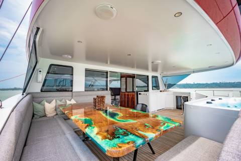 A stunning resin and wood dining table complements the luxurious outdoor seating area on this yacht, complete with a relaxing hot tub.