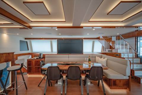 A luxurious yacht dining area features a polished wooden table, plush seating, and a large television, perfect for elegant onboard entertaining.