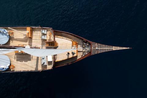 A luxurious wooden yacht glides across the deep blue sea, its deck adorned with comfortable seating and a billowing sail.