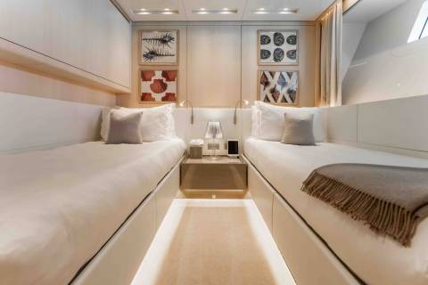 Two pristine beds with plush pillows and a cozy throw await weary travelers in this serene yacht cabin.