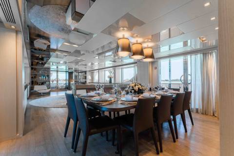 A luxurious dining room on a yacht features a beautifully set table with elegant lighting and large windows overlooking the water.