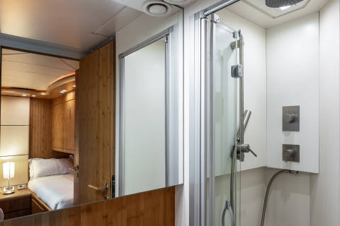 A luxurious yacht cabin features a sleek, modern shower stall adjacent to a cozy bedroom with warm wood accents.