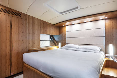 A luxurious bedroom features a large bed with white linens, a textured headboard, and warm wood paneling.