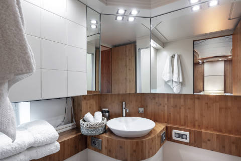 A modern yacht bathroom features a sleek white sink atop a curved wooden vanity, complemented by plush white towels and a mirrored wall.