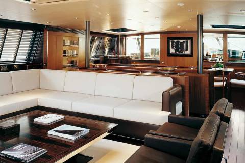Luxurious yacht interiors feature plush white sofas and dark leather armchairs around a polished wood coffee table.