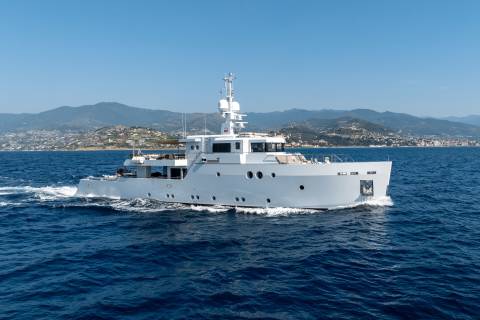 A sleek white yacht cruises through the deep blue sea with a lush, green coastline in the background.