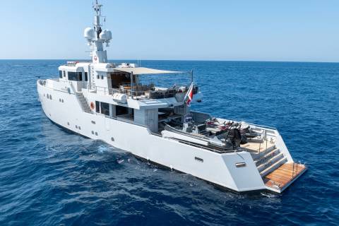 A sleek white yacht cruises on the deep blue sea, carrying jet skis and a tender on its expansive aft deck.