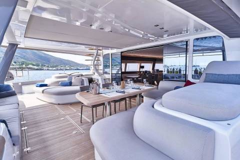 A luxurious and spacious interior of a yacht, featuring comfortable seating areas, a dining table, and large windows offering a scenic view of the surrounding mountains and water.