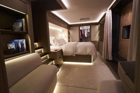A modern and cozy bedroom with a large bed, built-in shelves, and a seating area, all illuminated by warm, indirect lighting.