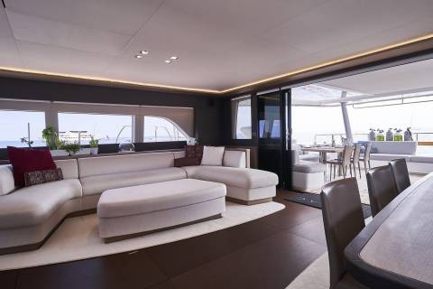 A modern and spacious living room with a large sectional sofa, a dining area, and large windows offering a scenic view of the outdoors.