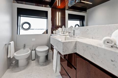 A luxurious yacht bathroom features a marble vanity, bidet, toilet, and a porthole window overlooking the sea.