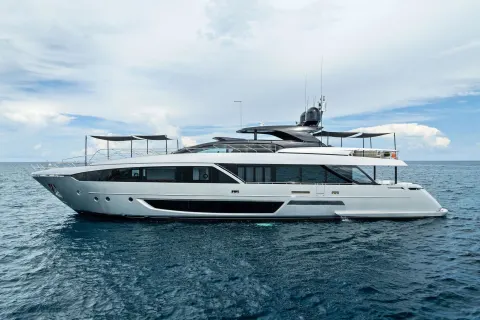 A sleek, modern yacht glides through the tranquil blue waters under a sky dotted with fluffy white clouds.