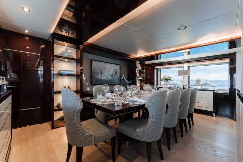 A luxurious dining room with a large wooden table surrounded by plush gray chairs, featuring a scenic view through the large windows in the background.