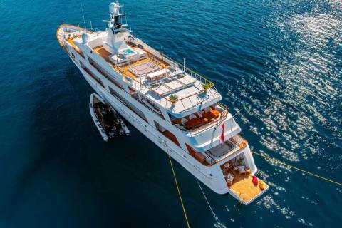 A luxurious white yacht with a tender boat alongside is anchored in the sparkling blue ocean.