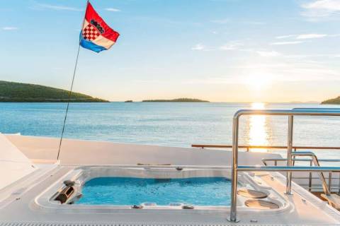 A Croatian flag flies proudly above a luxurious yacht's jacuzzi as the sun sets over the serene Adriatic Sea.