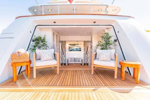 Relax in comfort on the teak deck of this luxurious yacht, surrounded by elegant seating and lush greenery.