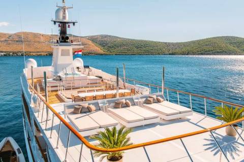 Luxurious sun loungers and a jacuzzi await on the deck of this yacht, anchored in the sparkling blue waters of a Mediterranean bay.