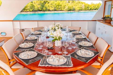 A beautifully set dining table awaits guests on a yacht deck, overlooking a serene blue bay.