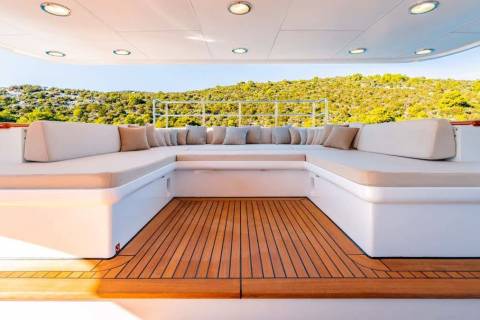 Luxurious U-shaped seating with plush cushions invites relaxation on this elegant yacht deck overlooking a verdant hillside.
