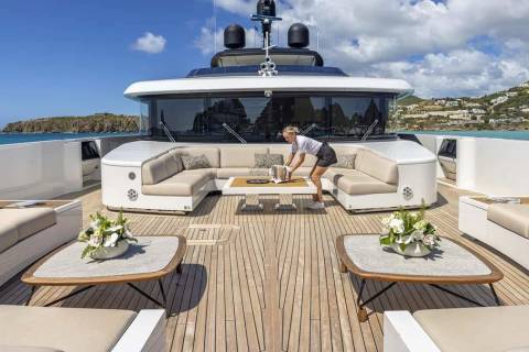 A woman arranges a bucket on a table in front of a large U-shaped sofa on a luxurious yacht's deck.