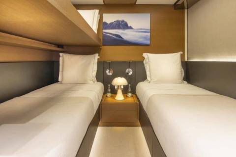 Twin beds in a cozy cabin are perfectly made with crisp white linens and a scenic mountain landscape above.