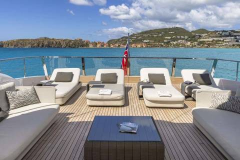 Relax on the spacious deck of a luxury yacht, surrounded by turquoise waters and a picturesque hillside town.