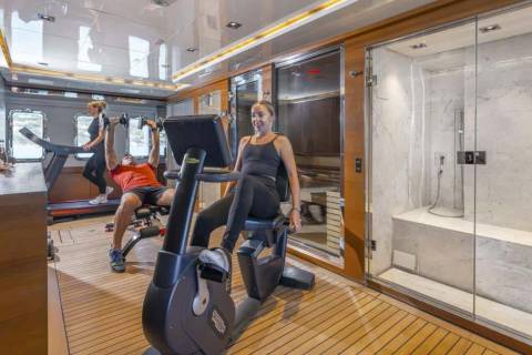 A couple enjoys a workout on a yacht's gym, complete with a treadmill, stationary bike, and a luxurious marble shower.