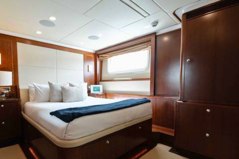 Luxurious yacht stateroom features a plush bed, rich wood paneling, and a private window with ocean views.