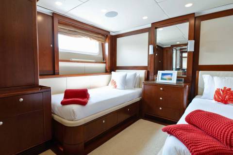 Cozy twin beds with red throws and nautical-themed pillows await in this luxurious yacht cabin.