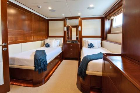 Luxurious twin beds with plush throws and coral-themed pillows create a serene retreat in this yacht's cabin.