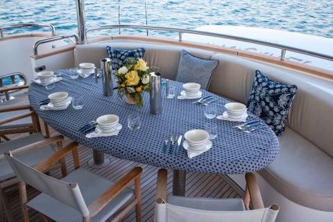 A beautifully set table awaits on a yacht's deck, ready for an al fresco meal with the ocean as a backdrop.