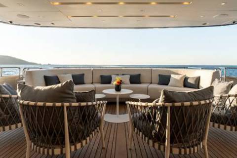 A luxurious outdoor seating area on the deck of a yacht, with comfortable wicker furniture and a stunning view of the ocean and mountains in the background.