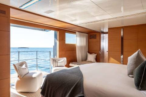 A cozy and luxurious bedroom with a panoramic view of the ocean, featuring a large bed, comfortable chairs, and a balcony overlooking the serene waters.