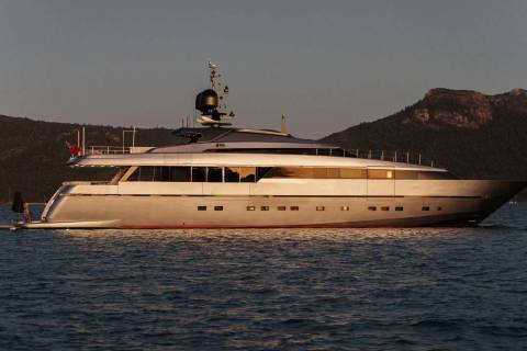 A large, luxurious yacht is anchored in a scenic body of water, surrounded by rugged mountains in the background.