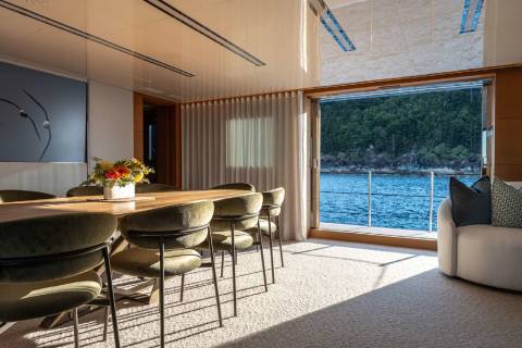A modern and stylish dining area with a large window overlooking a scenic body of water surrounded by lush greenery.