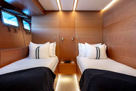 A cozy and well-appointed cabin interior with two twin beds, warm lighting, and a television mounted on the wall.