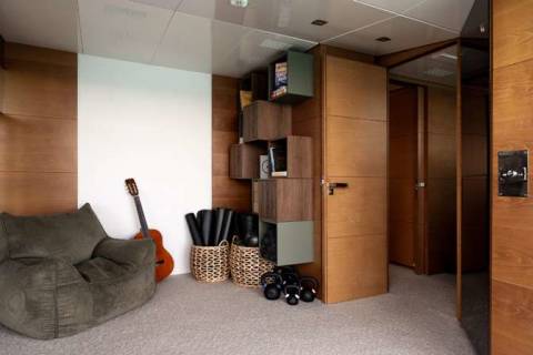 A cozy and cluttered living space with a gray bean bag chair, various storage containers, and a guitar in the foreground, set against a wooden and tiled background.