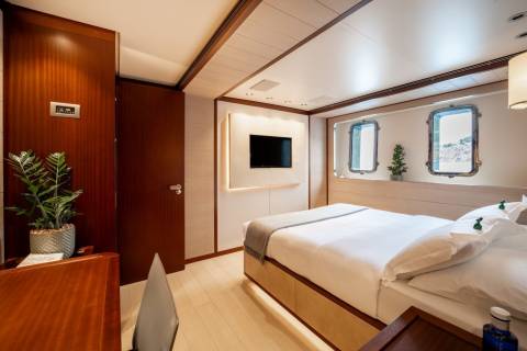 Luxurious cabin interiors feature polished wood, plush bedding, and scenic porthole views.
