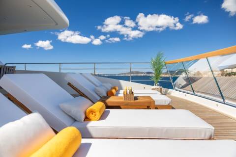 White lounge chairs and yellow towels await relaxation on a sun-drenched yacht deck overlooking the azure sea.