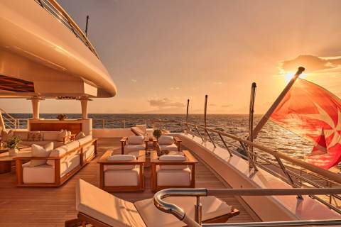 Golden hour bathes the luxurious deck of a yacht in warm light as the sun sets over the tranquil ocean.