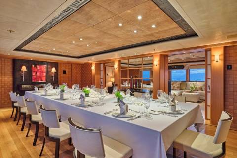 A formal dining table is set for a feast aboard a luxurious yacht, overlooking the ocean.